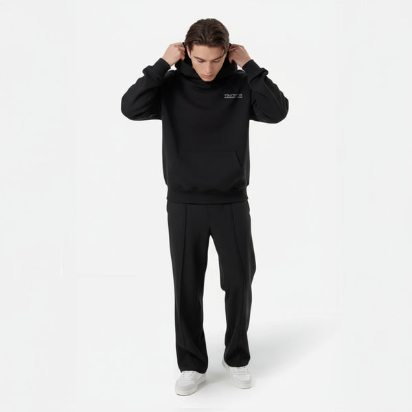 Homme en total look noir avec hoodie TOURISMO et baskets blanches, regard vers le sol