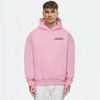 Homme portant un hoodie rose TOURISMO avec un pantalon blanc, look épuré