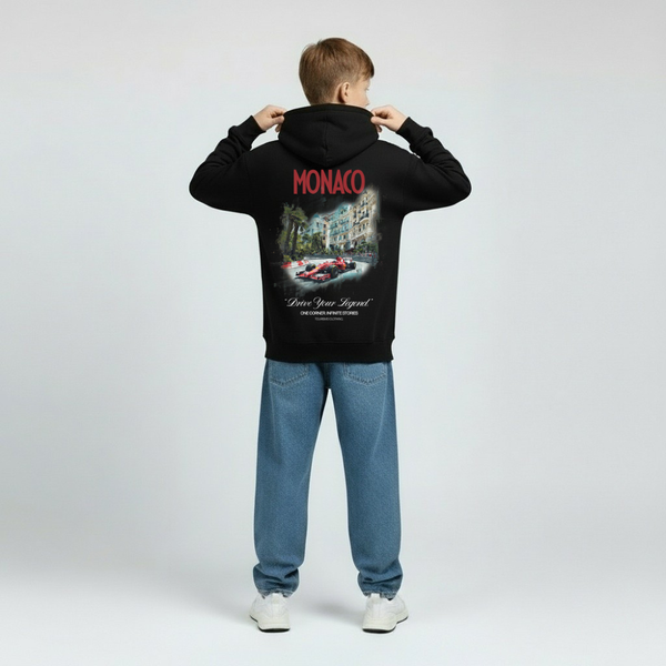 Hoodie noir enfant vu de dos, visuel Grand Prix de Monaco imprimé sur fond sombre, typographie blanche, éléments graphiques du circuit et de la ville. Capuche sur la tête, fond studio gris clair.