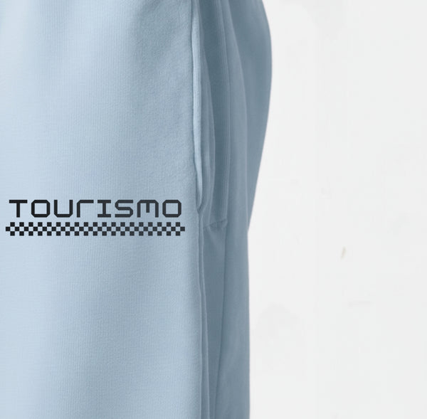 Gros plan sur le logo "Tourismo" blanc imprimé sur le pantalon de jogging bleu ciel.