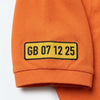 Nahaufnahme des am Ärmel gestickten Kennzeichens GB 07 12 25 auf dem Polo in Orange