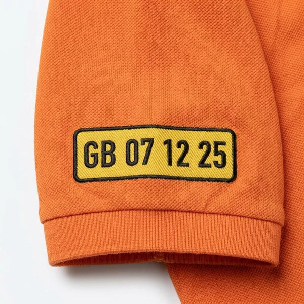 Nahaufnahme des am Ärmel gestickten Kennzeichens GB 07 12 25 auf dem Polo in Orange