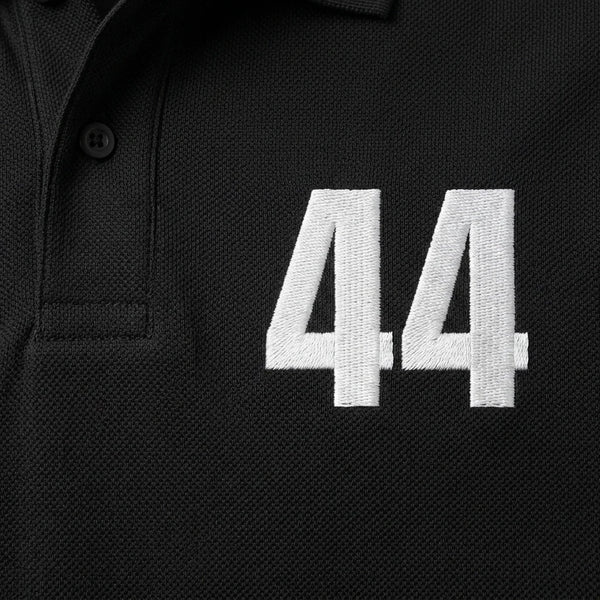 Nahaufnahme der weiß gestickten 44 auf dem Lewis Hamilton Polo in Schwarz